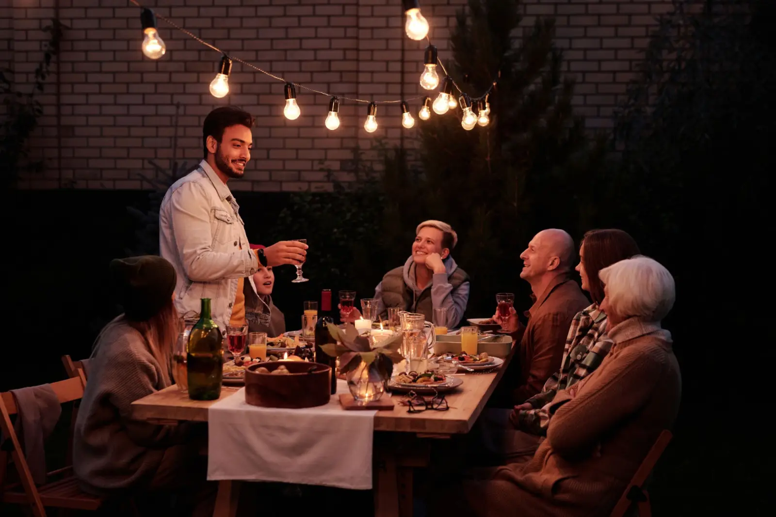 Friends at a long dinner table outside under string lights