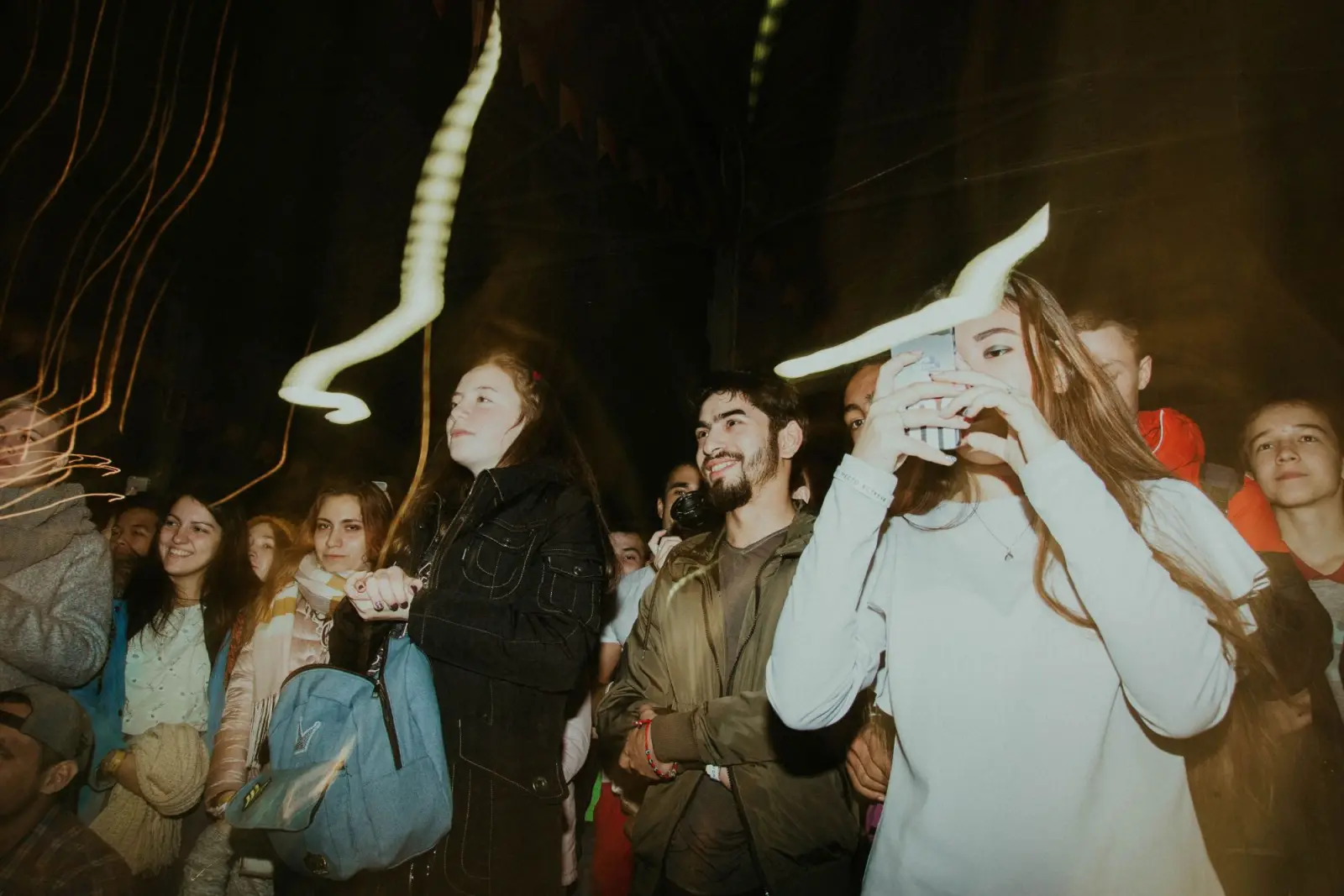 Friends in a crowd at night, one filming on her phone