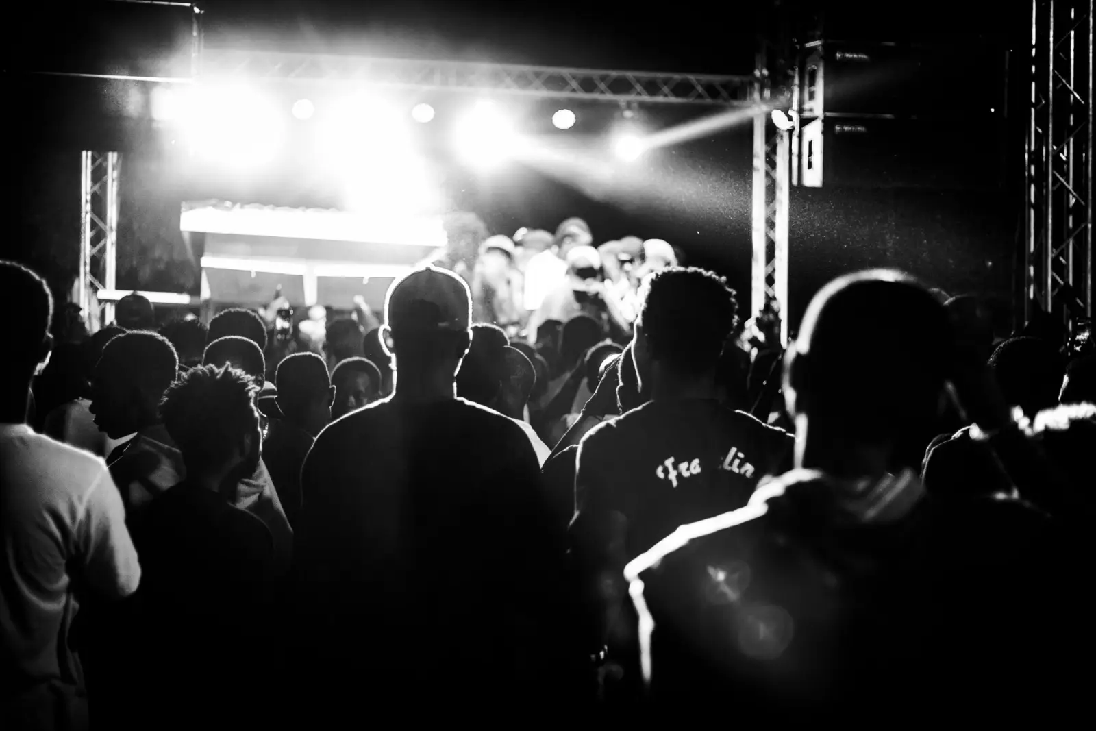 A crowd in front of a lit stage, in black and white